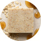 You will be generating high-quality product photos for an online stores product page. The product images should closely match the original products.
      Here is the prompt (IMPORTANT!): """Close-up of the 'Oatmeal Milk & Honey Soap' against a textured, c